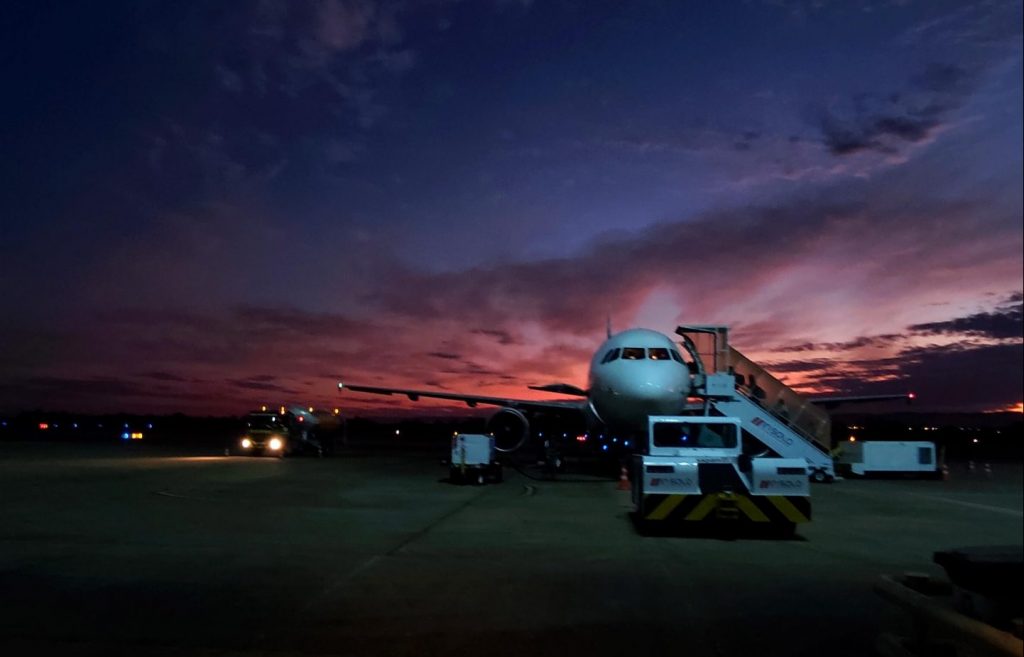 Foto do aeroporto, com o avião estacionado, e o céu colorido